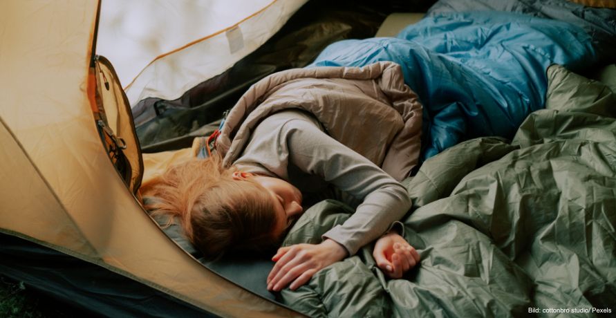 Person schläft im Schlafsack in einem Zelt